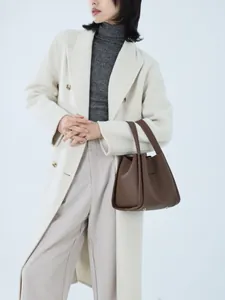 Close-up of brown litchi pattern leather bucket bag held by a model in a wool coat