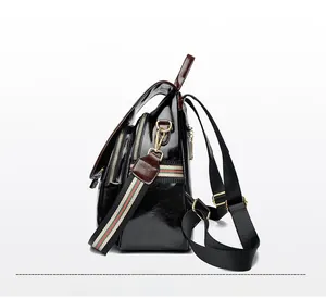 Detail of glossy black leather backpack with gold zippers and red-green striped strap