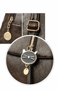 Detalle de bolso de cuero marrón oscuro con colgante de canguro dorado y dije de gato
