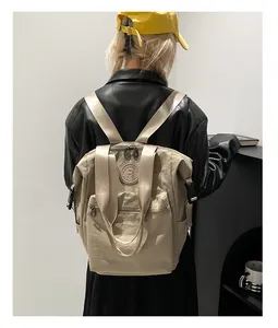 Rear view of a beige waterproof nylon backpack with multi-pocket design on a person