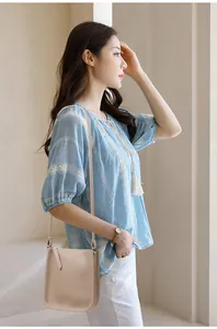 Detail of a beige litchi grain leather crossbody bag with a blue embroidered top