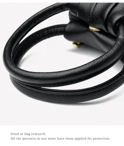 Détail d'un sac à main noir en cuir grainé avec poignées doubles et finitions dorées