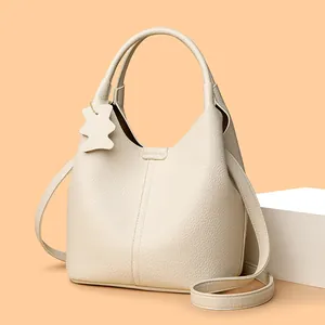 Elegant cream leather bucket bag with litchi texture and cute bear pendant accessory