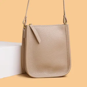 Minimalist beige pebble leather crossbody phone bag with U-shape design and gold hardware
