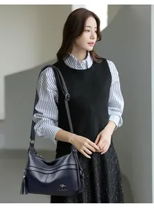 Deep blue leather crescent bag with lychee texture and decorative tassel on a model