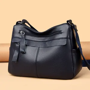 Dark blue leather crossbody bag with multiple zippers and wide strap on warm background