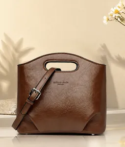 Detalle de un bolso cubo de cuero encerado marrón con asa troquelada y logotipo