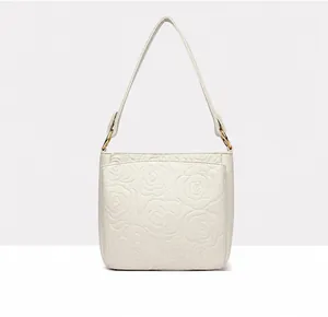 Detail view of the back side of a beige cowhide bucket bag with camellia floral embossing