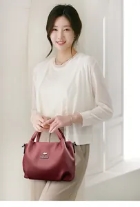 Detail of burgundy textured leather handbag with kangaroo logo shown by model