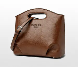 Detalle del bolso de mano en cuero marrón oscuro con textura de grano y correa ajustable