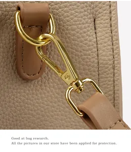 Macro detail of the golden lobster clasp and textured leather strap on a beige tote bag