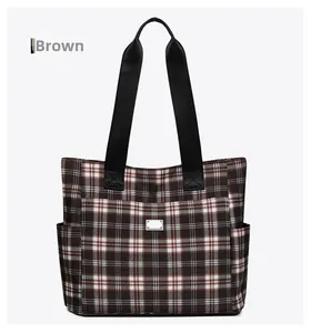 Détail frontal du sac cabas à carreaux marron avec poche avant et plaque en métal argenté