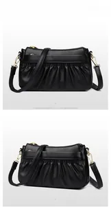 Detail of black leather crossbody bag with pleated texture and gold hardware accents