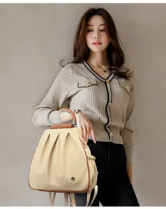 Detail of beige pleated backpack with leather trim and black camellia metal flower badge