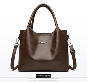 Détail de sac en cuir marron à motif litchi avec logo Yifutin en argent et bandoulière