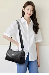 Detail of woven leather crossbody bag with circular metal logo and adjustable wide strap