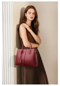 Detail of burgundy leather tote bag with pebble texture and triangular metal pendant