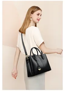 Model wearing a black lychee texture leather tote bag with gold metal V-shaped pendant