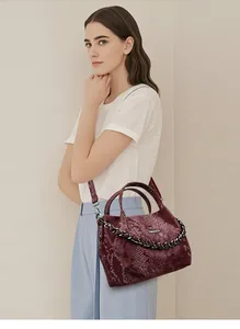 Detail of burgundy snakeskin texture on handbag with gold kangaroo logo and thick chain