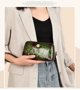 Detail of dark green embossed floral leather clutch with gold clasp held by a model