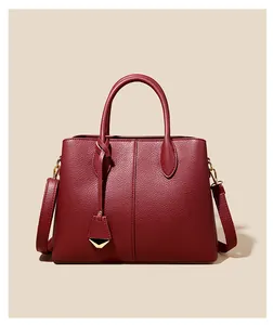 Detail of deep red lychee grain leather handbag with gold metal pendant and dual handles