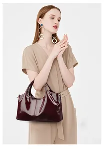 Detailansicht einer glänzenden weinroten Lacklederhandtasche, gehalten von einem Model
