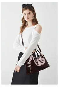 Detailansicht der weinroten Lacklederhandtasche mit Goldbeschlägen und Schultergurt