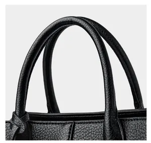 Detailed macro view of black pebbled leather texture and reinforced stitching on tote handle