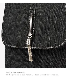 Detailed shot of black denim bag flap with white contrast stitching and silver chain tassels
