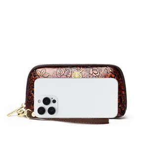 Vintage brown leather clutch with rose embossing and wristlet next to a smartphone