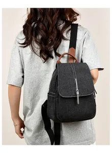 Close-up of black denim backpack featuring brown leather straps and silver chain tassel detail