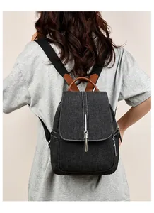 Detail of a black denim backpack featuring chain tassels and brown leather handle