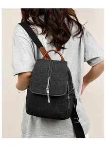 Detail shot of a black denim backpack with metal chains, tassels and brown leather handle