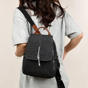 Denim backpack with metal chain tassels and leather handle shown on model's back