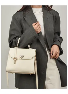 Detailansicht einer weißen Ledertasche mit Narbenstruktur und goldenem Rundschloss-Anhänger