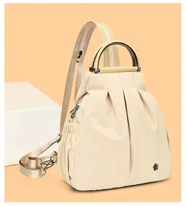 Detail eines cremefarbenen Plissee-Rucksacks mit rundem Metallgriff und floralem Akzent