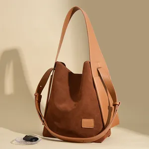 Brown suede leather bucket tote bag with wide shoulder strap in minimalist lighting