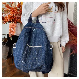 Detail of blue denim backpack showing embroidered diamond lattice pattern and side pocket