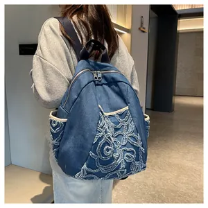 Detailed close-up of blue denim backpack featuring 3D floral embroidery and dual zippers