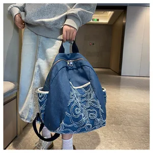 Detailed close-up of blue denim backpack showing floral embroidery and silver dual zippers