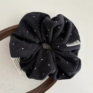 Macro detail of dark grey polka dot hair scrunchie with wool texture and woven label