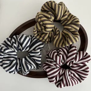 Three striped knitted scrunchies in black, yellow, and red colors on a wooden tray