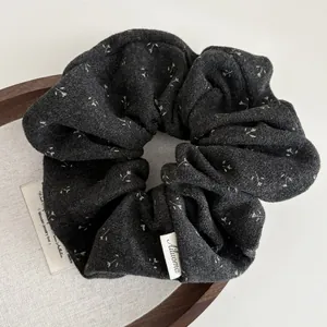 Détail d'un chouchou en tricot gris à fleurs avec texture douce et logo Ailuoma