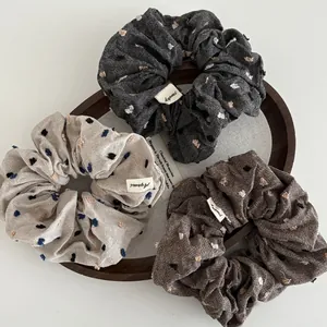 Three-piece set of textured scrunchies in brown, beige, and grey with cute pom-pom dots