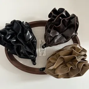 Close-up of pleated PU leather banana hair clips in black, brown, and khaki colors