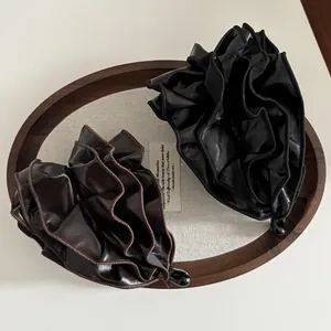 Detailed view of layered pleats on leather banana hair clips in black and dark brown
