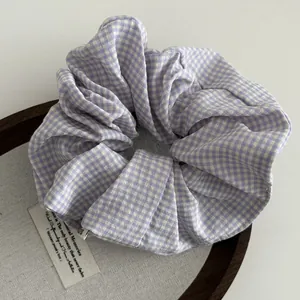 Detailopname van paarse gingham scrunchie met zachte stof op houten dienblad