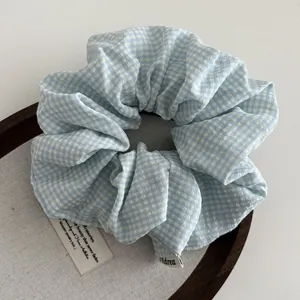 Detailweergave van de blauw-witte ruitjes scrunchie met Andrea geweven label