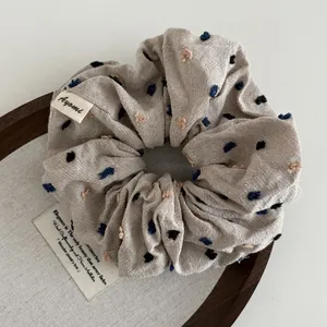 Macro view of beige scrunchie with colorful embroidered dots and brand label detail