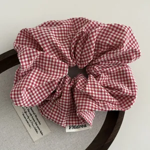 Detail van rood-wit geruite scrunchie met merklabel op een houten standaard